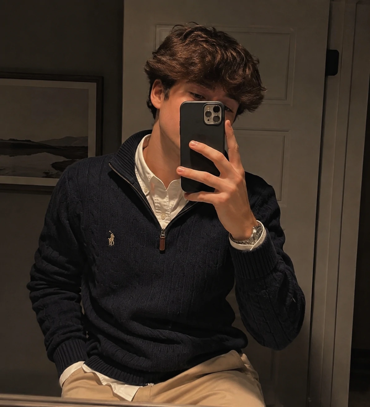 Preppy pfp boy in a mirror selfie with a casual layered outfit and soft warm lighting